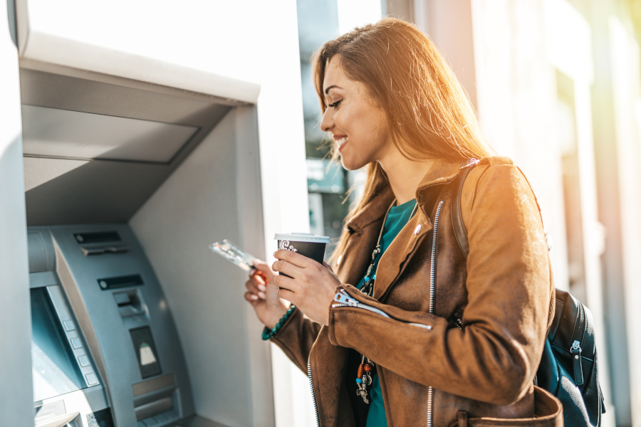Усмихната жена тегли пари от банкомат с картата си.